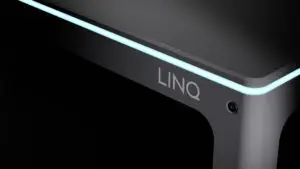 A dark image of the Automata LINQ bench that shows the name 'LINQ' on the front of it. There is a light blue LED light around the edge of the bench.