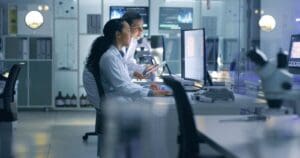 Stock image of scientists in a laboratory looking at results on a lab computer.