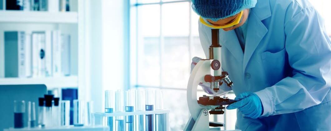 Scientist in PPC looking through a microscope in a life sciences lab